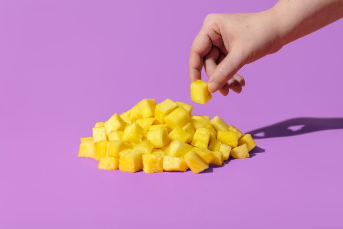 Hand taking a piece of pineapple from pile of chunks
