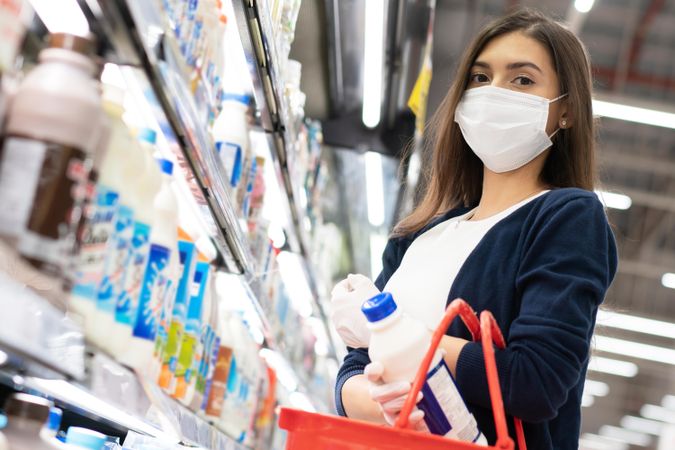 Woman picking up milk at grocery shopping in surgical mask
