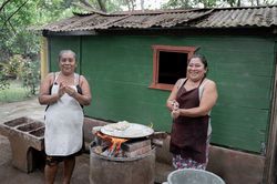 Two adult Hispanic women are smiling while shaping corn tortillas by hand