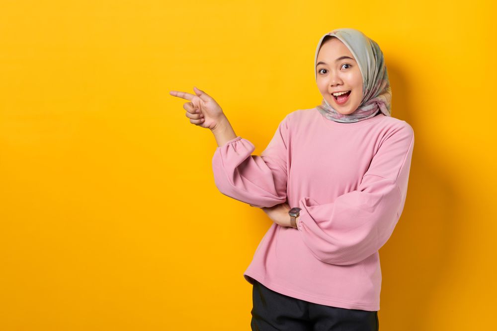 Excited Muslim woman in head scarf pointing to her side
