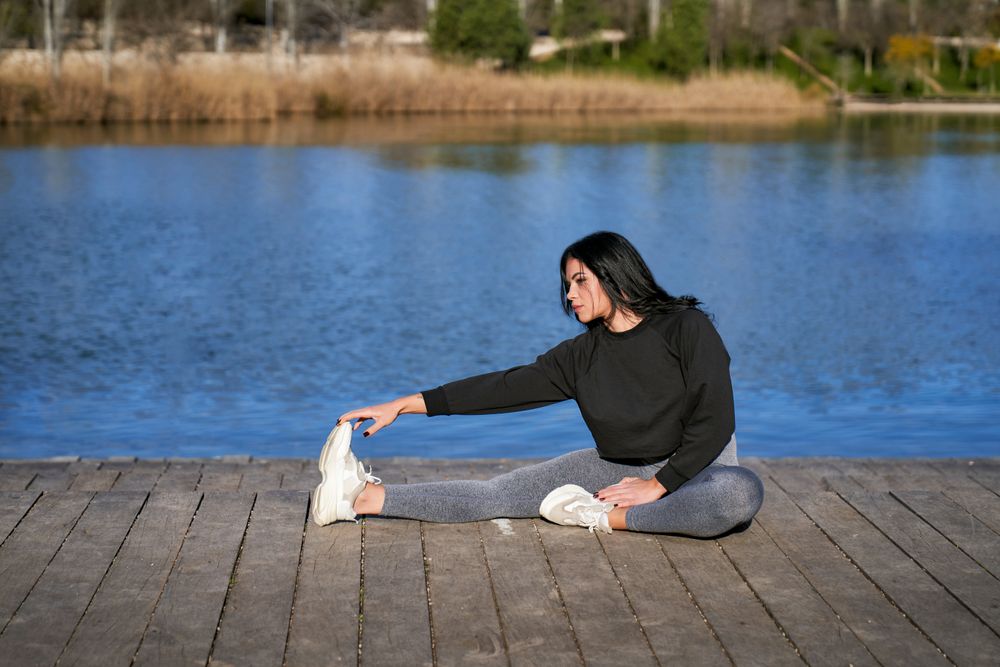 a young sportswoman stretches while sitting on a lake jetty