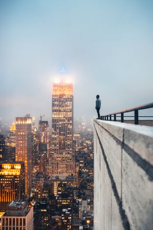 Man in dark jacket standing on the edge of a high rise building in city