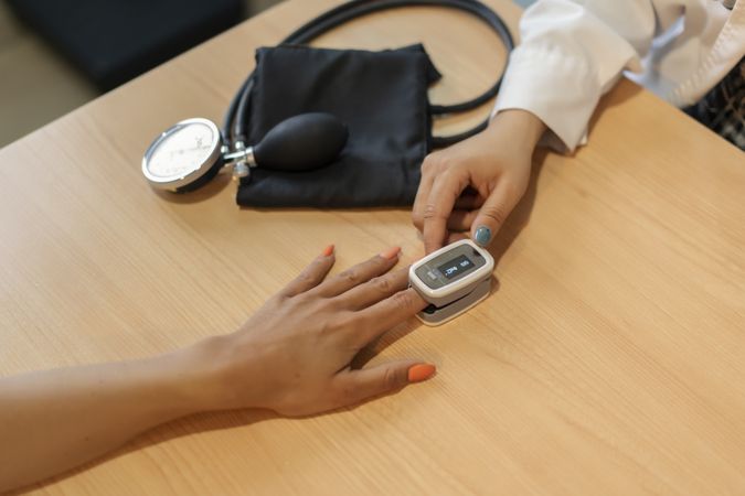 Doctor near hand of patient with tonometer at table with pulsometer