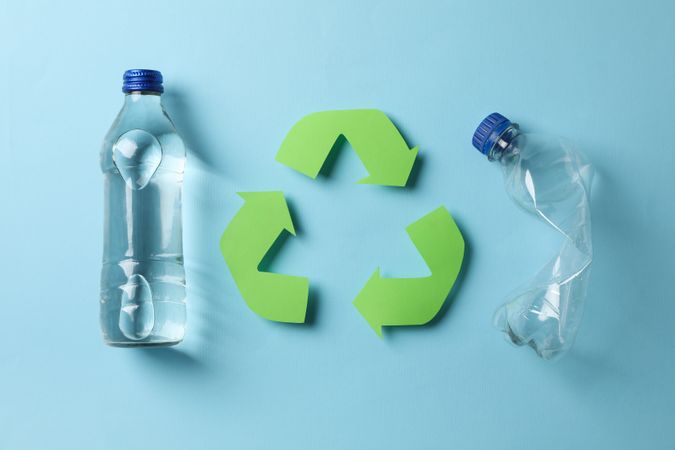 Glass and plastic water bottle with recycling symbol in blue room