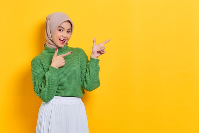 Excited woman in headscarf pointing both her finger towards the side