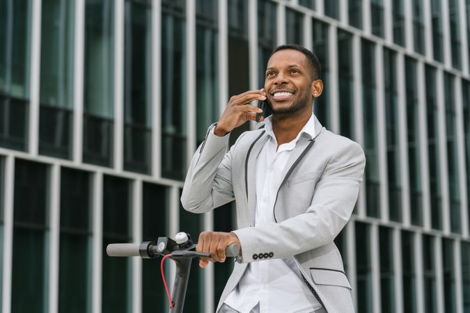 Smiling Black man riding scooter and speaking on smartphone
