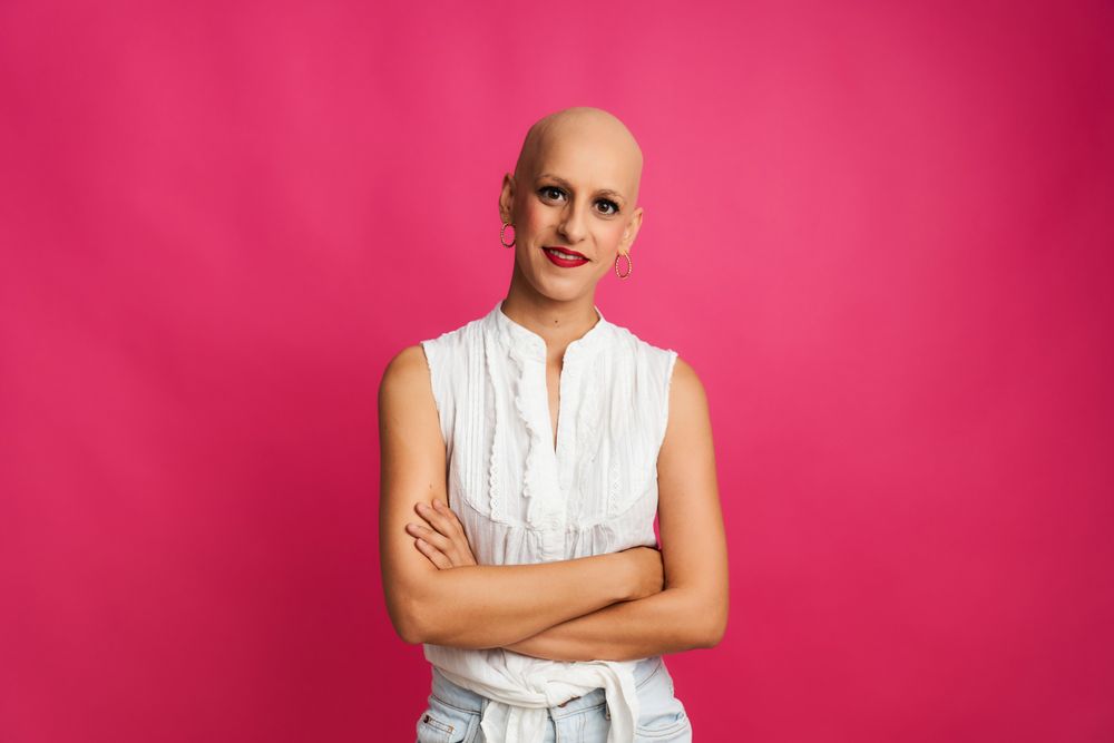 portrait of a woman with cancer with hairless head and crossed arms on pink background