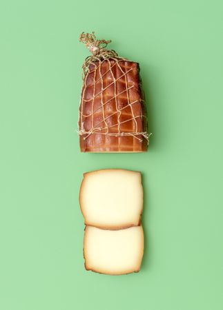 Sliced smoked cheese above view, minimalist on a green background