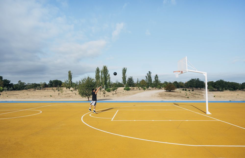 Young man playing on yellow basketball court outdoor.