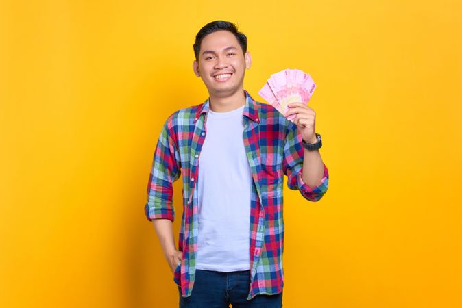 Smiling confident Asian man with cash in one hand in studio shoot