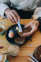 Tattooed hand spreading butter on grainy toast