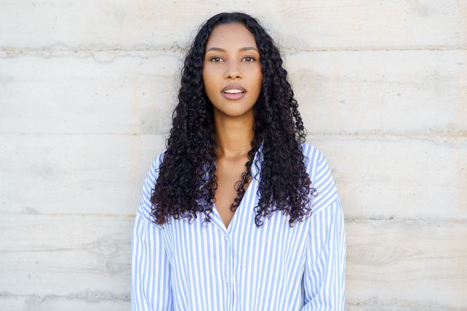 A Confident Young Woman with Beautiful Curly Hair Posing Delightfully Against a Textured Background