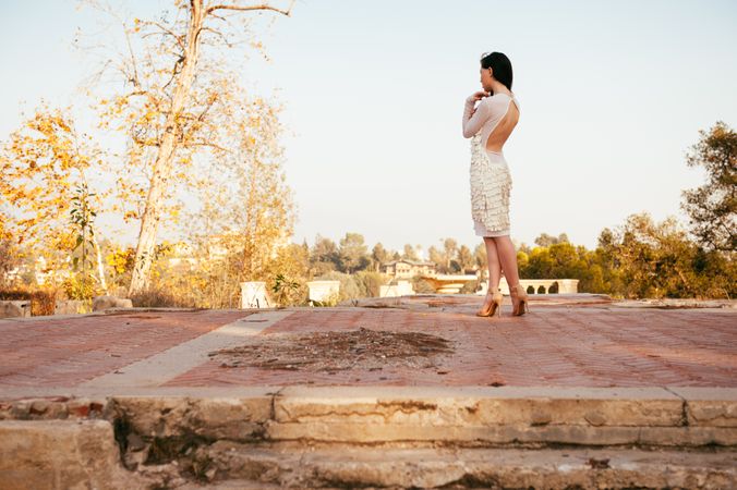 Woman in white dress with ruffles standing on stone foundation looking away from camera