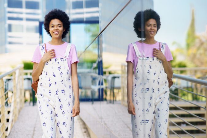 Amused female in floral overalls walking outside past corporate building