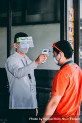 Security guard using thermometer on customer's head to measure his temperature 4Z7qOb