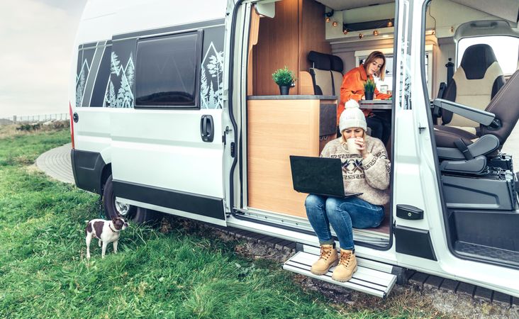 Female in sweater working remotely sitting on step of van while on a road trip