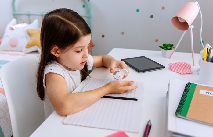 Girl applying hand sanitizer while doing homework