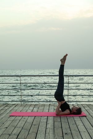 Woman on yoga mat on wooden floor at sea, space for text