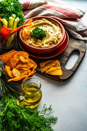 Creamy hummus dip with chips and vegges on bread board