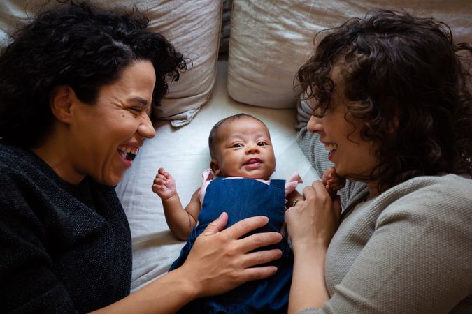 Mom resting her hand on baby’s belly with another mom smiling