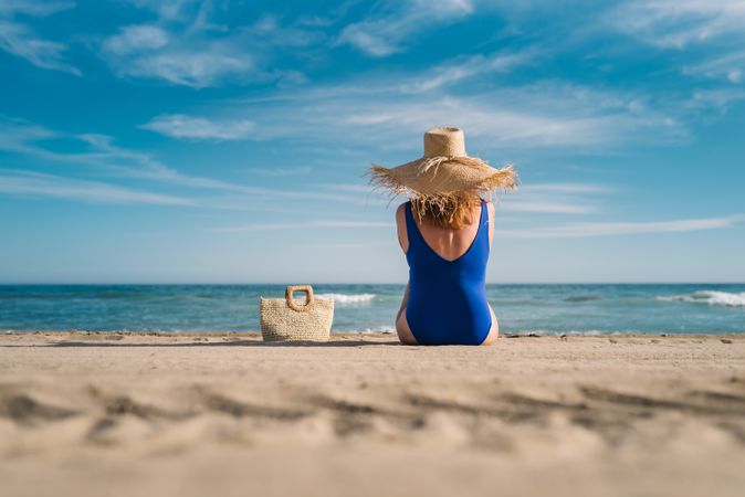 Woman in blue swimsuit and hat on sandy beach