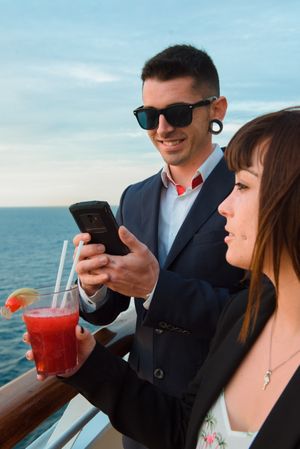 Couple on mobile phone and drink on deck of ship