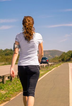Back of woman in athletic gear walking along road, vertical