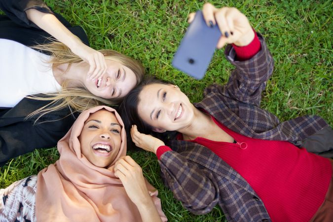 Looking down at three women lying on grass with phone