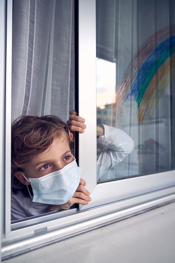 Boy in medical mask looking out window