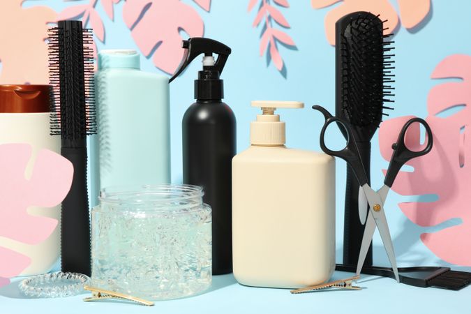 Composition with hairdressing accessories and paper palm leaves on blue background