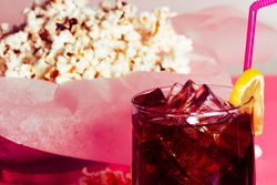 Popcorn in bowl near drink in glass with ice and lemon