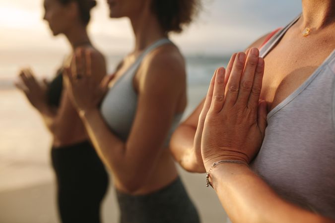Three women in fitness wear doing yoga and meditation standing at the seashore