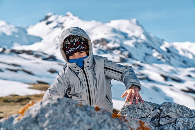 Boy climbing on rock in snowy mountains