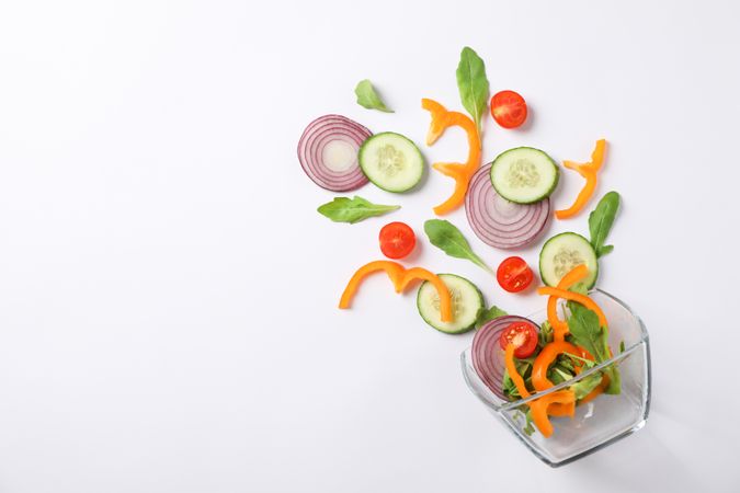 Glass bowl with fresh vegetables slices on blank background, copy space