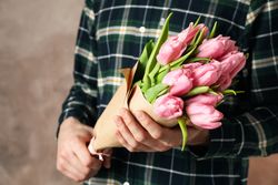 Man in shirt holding bouquet of tulips on brown background, close up