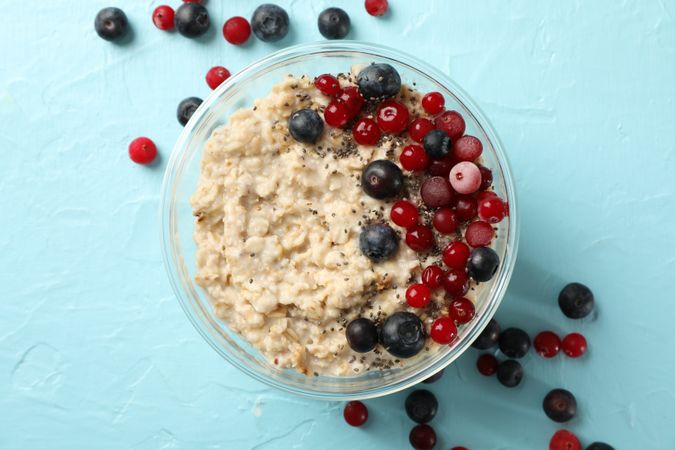 Bowl with oatmeal porridge and fruits on blue background