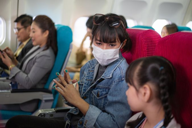 Woman in facemark sitting on flight with little girl