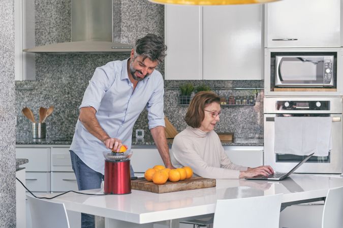 Smiling adult son making orange juice near mature mother in kit