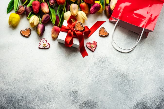 Tulips, shopping bag and checkered heart ornaments with present on grey counter