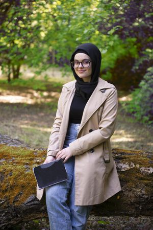 Middle Eastern woman sitting on fallen tree smiling with book