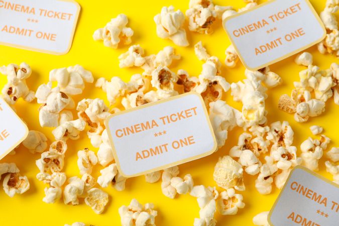 Popcorn and cinema tickets on yellow background, close up
