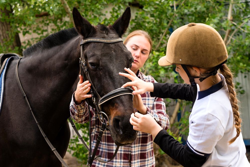 Woman and young rider adjusting bridle on horse.