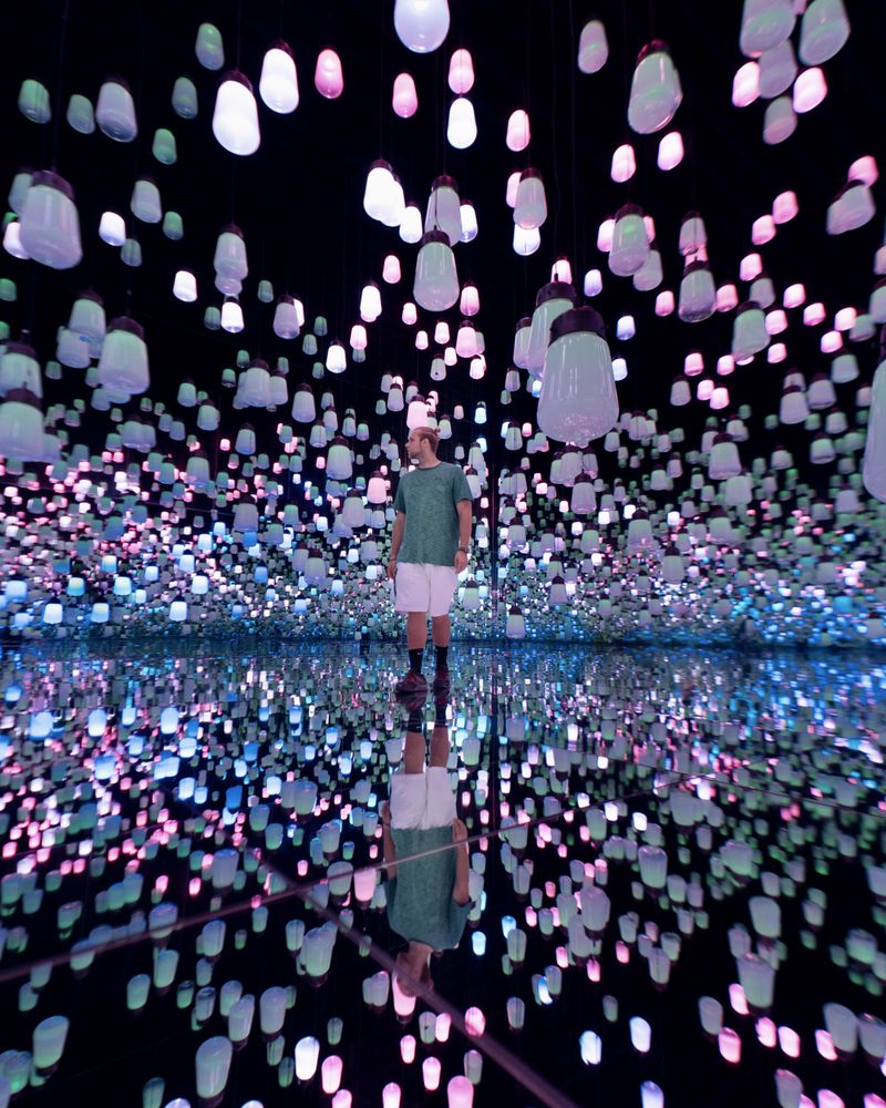 Man standing in a room with illusion of light paper lanterns in ceiling reflected on mirror floor