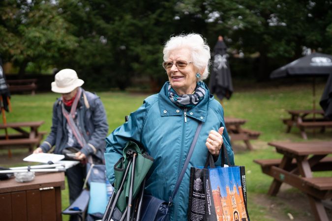 Grey haired woman walking away from park benches with picnic supplies