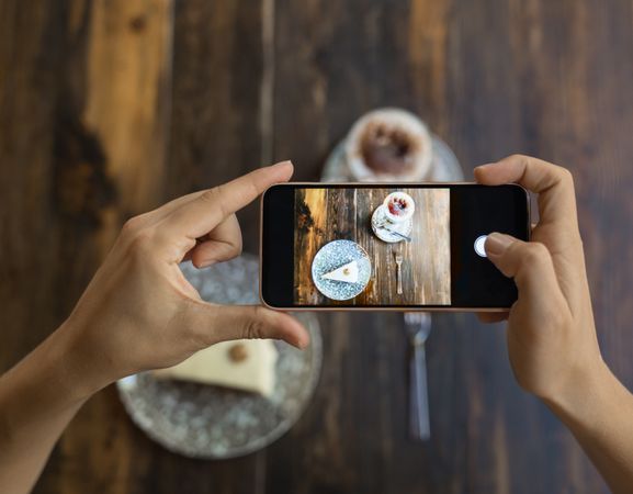 Faceless person taking picture of cake and coffee