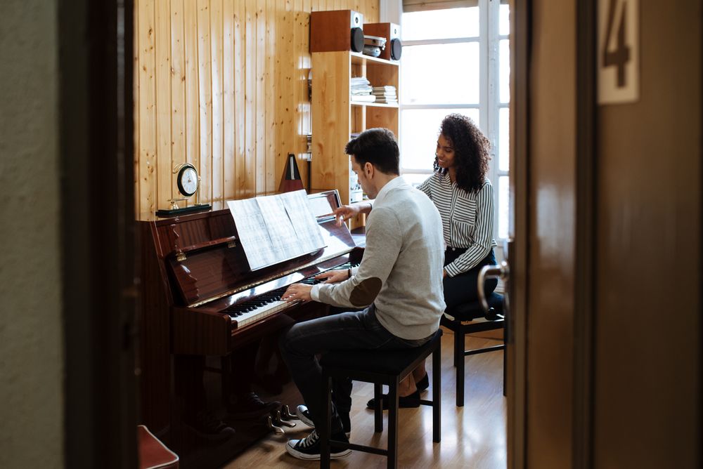 Man playing piano near woman teaching in studio