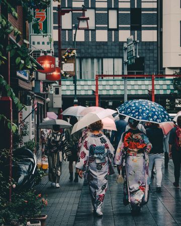 Back view of woman in kimonos holding umbrellas walking on street