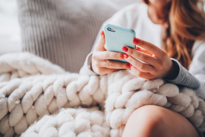 Woman under a cozy blanket checking her cell phone