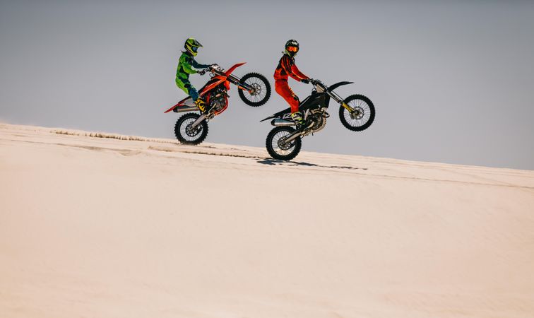 Two motocross racers doing synchronized wheelie in desert