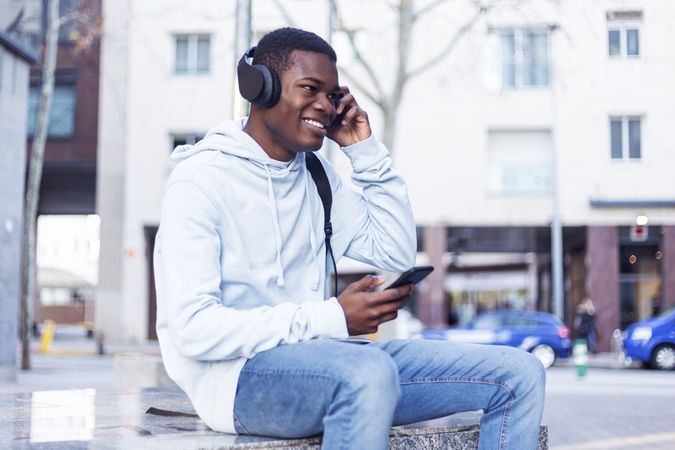 Happy man sitting in the street while listening music on headphones